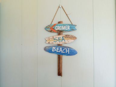 A wooden sign with arrows reading cromer sea beach hanging on a wall at The Beach Hut in Cromer