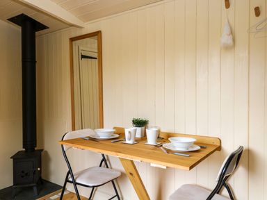 A small dining area with a wooden table set for two and a black wood stove at Mitford Gypsy Hut in Moreton-In-Marsh