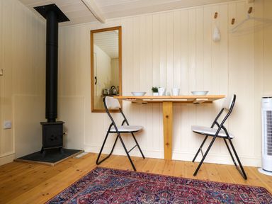 A small dining area with a wooden wall mounted table two folding chairs a wood stove and a mirror at Mitford Gypsy Hut in Moreton-In-Marsh