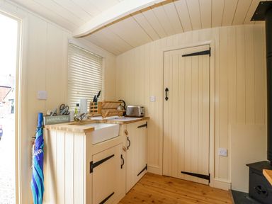 A small kitchen corner with a sink, dish rack, toaster, and an umbrella leaning against the counter at Mitford Gypsy Hut in Moreton-In-Marsh