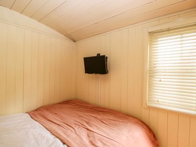 A small bedroom with a bed covered by a reddish blanket and a wall-mounted television at Mitford Gypsy Hut in Moreton-In-Marsh