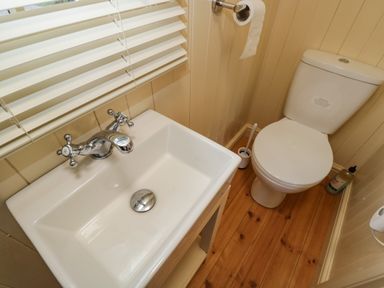 A small bathroom with a white sink wooden floor and a white toilet at Mitford Gypsy Hut in Moreton-In-Marsh