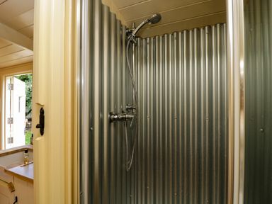A bathroom with a corrugated metal shower enclosure and a window with an open door at Mitford Gypsy Hut in Moreton-In-Marsh