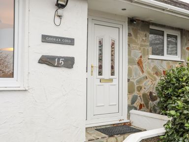The entrance door of a house with a white door and stained glass panels next to a stone wall with house number 15 at 15 Maes Awel in Abersoch