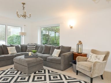 A living room with a grey sectional sofa a beige armchair and a black and white patterned rug at 15 Maes Awel in Abersoch