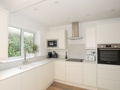 A kitchen with white cabinets a window with a plant coffee machine kettle toaster built in oven and stovetop at 15 Maes Awel in Abersoch