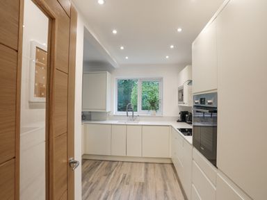 A kitchen with white cabinets a sink under a window and wooden flooring at 15 Maes Awel in Abersoch