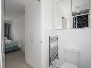 A view of a bathroom with a toilet and towel warmer next to a hallway leading to a bedroom with a bed and wardrobe at 15 Maes Awel in Abersoch