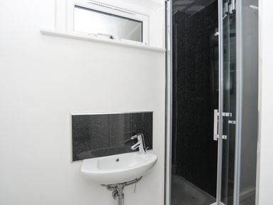 A small bathroom with a white wall mounted sink and a shower with glass doors at 15 Maes Awel in Abersoch