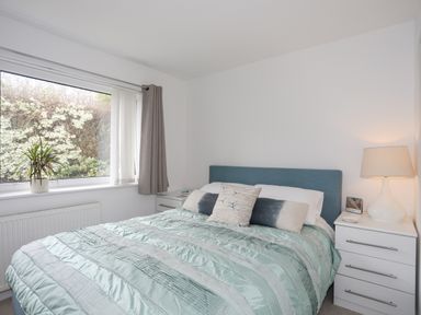 A bedroom with a bed a window with curtains and a bedside table with a lamp at 15 Maes Awel in Abersoch