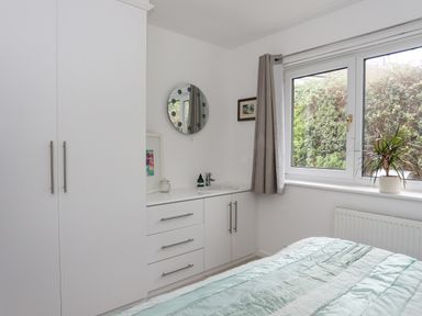 A bedroom with built in white cupboards a round mirror a window and a bed at 15 Maes Awel in Abersoch