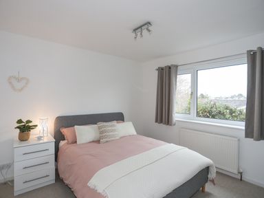A bedroom with a bed with pink bedding and pillows next to a dresser and window at 15 Maes Awel in Abersoch