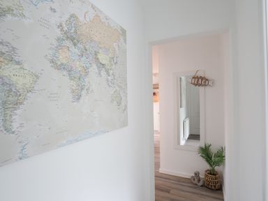 A hallway with a world map on the wall and a mirror with a sign that reads beach next to a plant at 15 Maes Awel in Abersoch