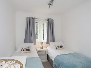 A bedroom with two single beds and a nightstand with a lamp at 15 Maes Awel in Abersoch