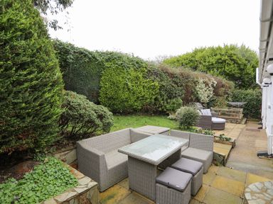 An outdoor patio area with a wicker dining set including a table and chairs surrounded by greenery at 15 Maes Awel in Abersoch