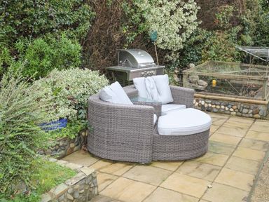 A patio with a round wicker sofa with cushions a barbecue grill and plants at 15 Maes Awel in Abersoch