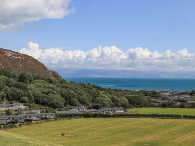 A coastal landscape with a green field trees houses and the sea at 15 Maes Awel in Abersoch