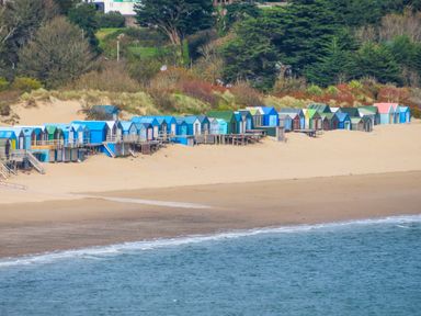 A row of colorful beach huts on sand near the sea with trees in the background at 15 Maes Awel in Abersoch
