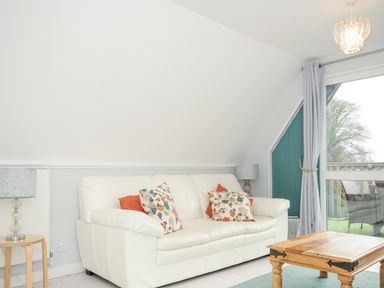 A living room with a white sofa with floral cushions a wooden coffee table two lamps and a sliding glass door at 24 Valley Lodge in Honicombe Park near Drakewalls