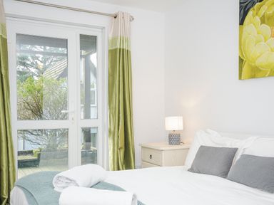 A bedroom with a bed white linens a bedside table with a lamp and green curtains at 24 Valley Lodge in Honicombe Park near Drakewalls