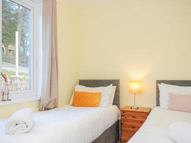 A bedroom with two single beds with pillows bedside table with lamp and window with curtains at 24 Valley Lodge in Honicombe Park near Drakewalls