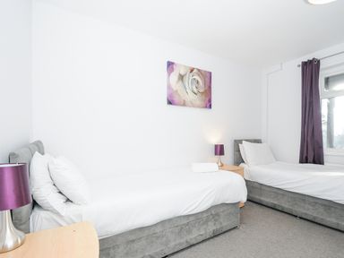 A bedroom with two single beds bedside tables purple lamps and a window with purple curtains at 24 Valley Lodge in Honicombe Park near Drakewalls