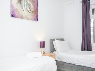 A bedroom with two single beds separated by a wooden nightstand with a purple lamp and a framed rose picture on the wall at 24 Valley Lodge in Honicombe Park near Drakewalls