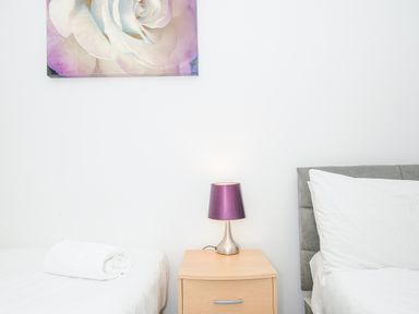 A bedroom with two beds a wooden nightstand and a lamp with a purple shade at 24 Valley Lodge in Honicombe Park near Drakewalls