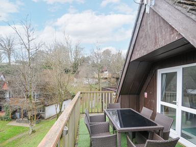 An outdoor balcony with a glass table and six wicker chairs surrounded by wooden railing at 24 Valley Lodge in Honicombe Park near Drakewalls