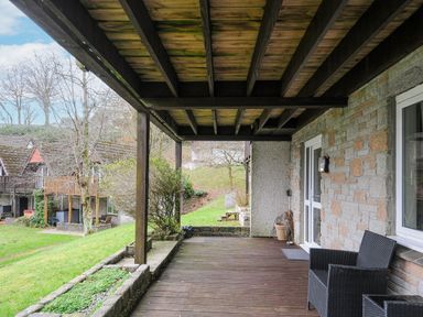 A covered wooden deck with a black chair and stone walls at 24 Valley Lodge in Honicombe Park near Drakewalls