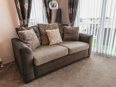 A sofa with cushions near windows with blinds and patterned curtains at Evergreen Pines in Cayton Bay near Scarborough