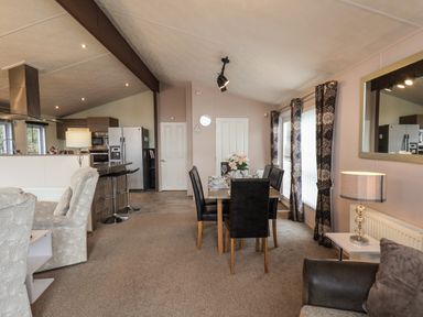 An open plan dining and kitchen area with a dining table and chairs a sofa and a breakfast bar with stools at Evergreen Pines in Cayton Bay near Scarborough