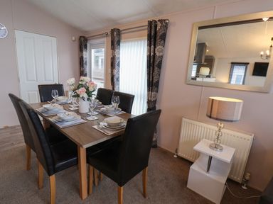 A dining room with a table set for six people a vase of flowers on the table black chairs and a lamp on a side table at Evergreen Pines in Cayton Bay near Scarborough