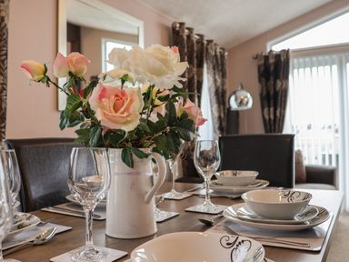 A dining table set with plates bowls wine glasses and a vase of flowers at Evergreen Pines in Cayton Bay near Scarborough