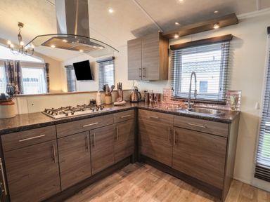 A kitchen with wooden cabinets a gas stove a metal range hood a sink and windows with blinds at Evergreen Pines in Cayton Bay near Scarborough