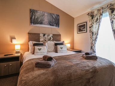 A bedroom with a double bed two bedside tables and lamps forest picture above the bed and curtains on the window at Evergreen Pines in Cayton Bay near Scarborough
