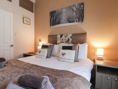 A bedroom with a double bed with pillows and folded towels on it two bedside tables with lamps and artwork on the walls at Evergreen Pines in Cayton Bay near Scarborough
