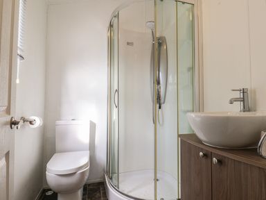 A bathroom with a toilet a corner shower with glass doors and a sink on a wooden cabinet at Evergreen Pines Cayton Bay near Scarborough