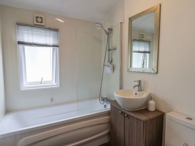 A bathroom with a bathtub shower combination a sink on a wooden cabinet a mirror and a window at Evergreen Pines in Cayton Bay near Scarborough