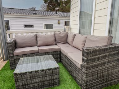 An outdoor corner sofa with beige cushions and a glass top coffee table on artificial grass at Evergreen Pines in Cayton Bay near Scarborough