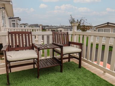 A small outdoor deck with two wooden chairs with cushions and a table between them at Evergreen Pines in Cayton Bay near Scarborough
