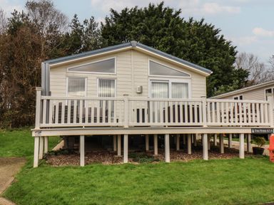 A raised mobile home with a white railing and green grass in the foreground at Evergreen Pines in Cayton Bay near Scarborough