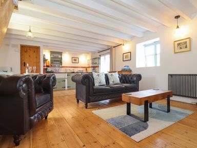 A living room with leather couches and a wooden coffee table next to a kitchen area at Oofoo's Barn in Mullion