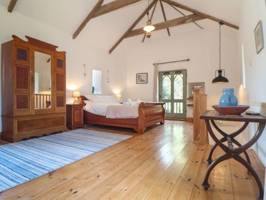 A bedroom with a wooden bed two bedside tables a wardrobe a blue striped rug and a small table with a blue vase at Oofoo's Barn in Mullion