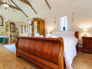 A bedroom with a wooden sleigh bed bedside tables lamps an armoire and a partially visible bathroom at Oofoo's Barn in Mullion