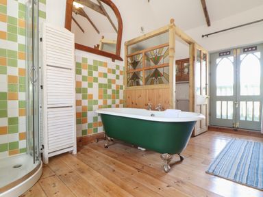 A bathroom with a green clawfoot bathtub a shower with glass door tiled walls and wooden floor at Oofoo's Barn in Mullion