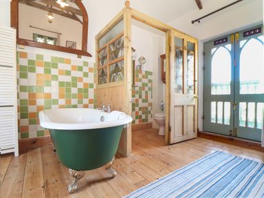 A bathroom with a green clawfoot bathtub wooden floor and a tiled wall at Oofoo's Barn in Mullion