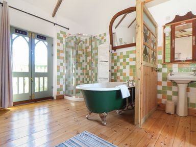 A bathroom with a green clawfoot tub a glass shower a wooden floor and a sink with mirror at Oofoo's Barn in Mullion