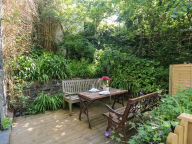 A garden with a table and benches surrounded by greenery at Oofoo’s Barn in Mullion