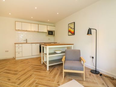 A kitchen with white cabinets a wooden countertop a gray armchair a black floor lamp and a framed picture on the wall at Valise in Bideford